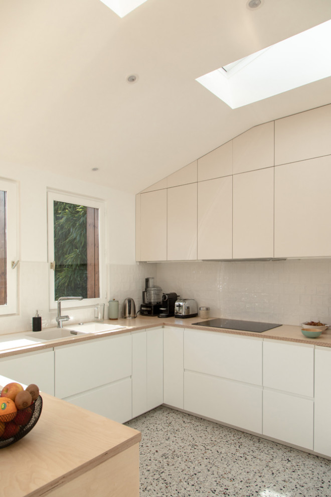 Photo of a large modern u-shaped kitchen/diner in Paris with a built-in sink, flat-panel cabinets, white cabinets, wood worktops, beige splashback, terracotta splashback, integrated appliances, terrazzo flooring, a breakfast bar, multi-coloured floors and beige worktops.