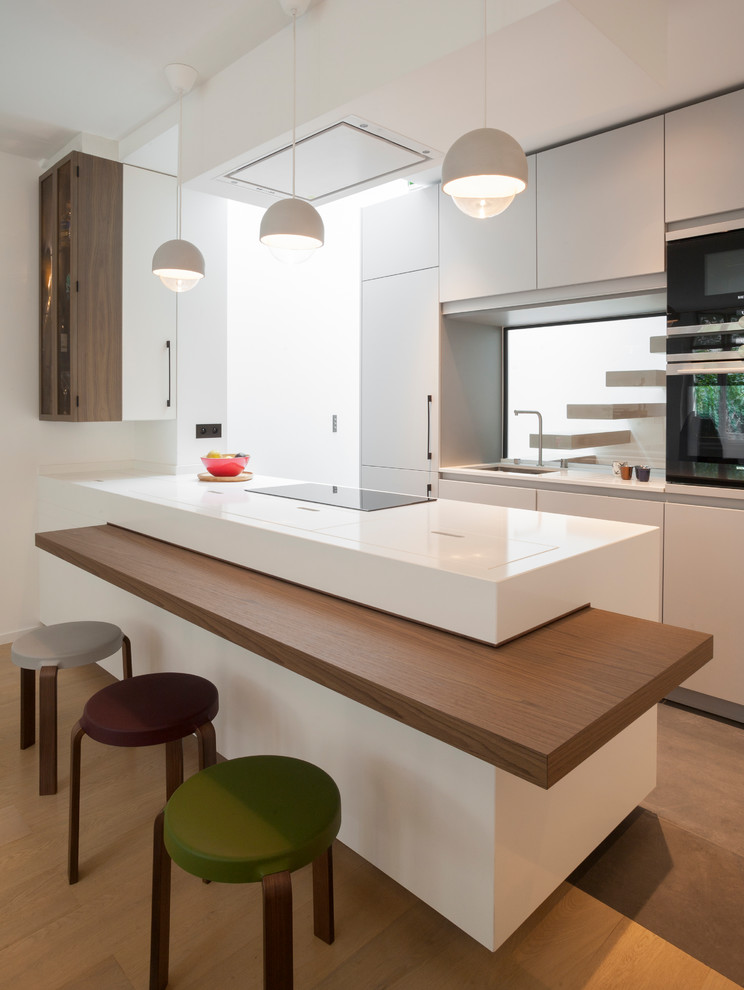 Photo of a contemporary kitchen in Paris with a submerged sink, flat-panel cabinets, white cabinets, window splashback, black appliances, a breakfast bar, brown floors and white worktops.