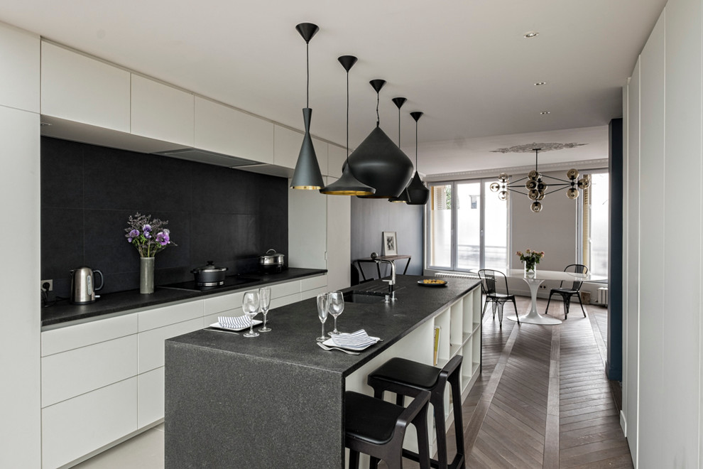 Zweizeilige, Große Moderne Wohnküche mit Unterbauwaschbecken, Küchenrückwand in Schwarz, Elektrogeräten mit Frontblende, braunem Holzboden und Kücheninsel in Paris