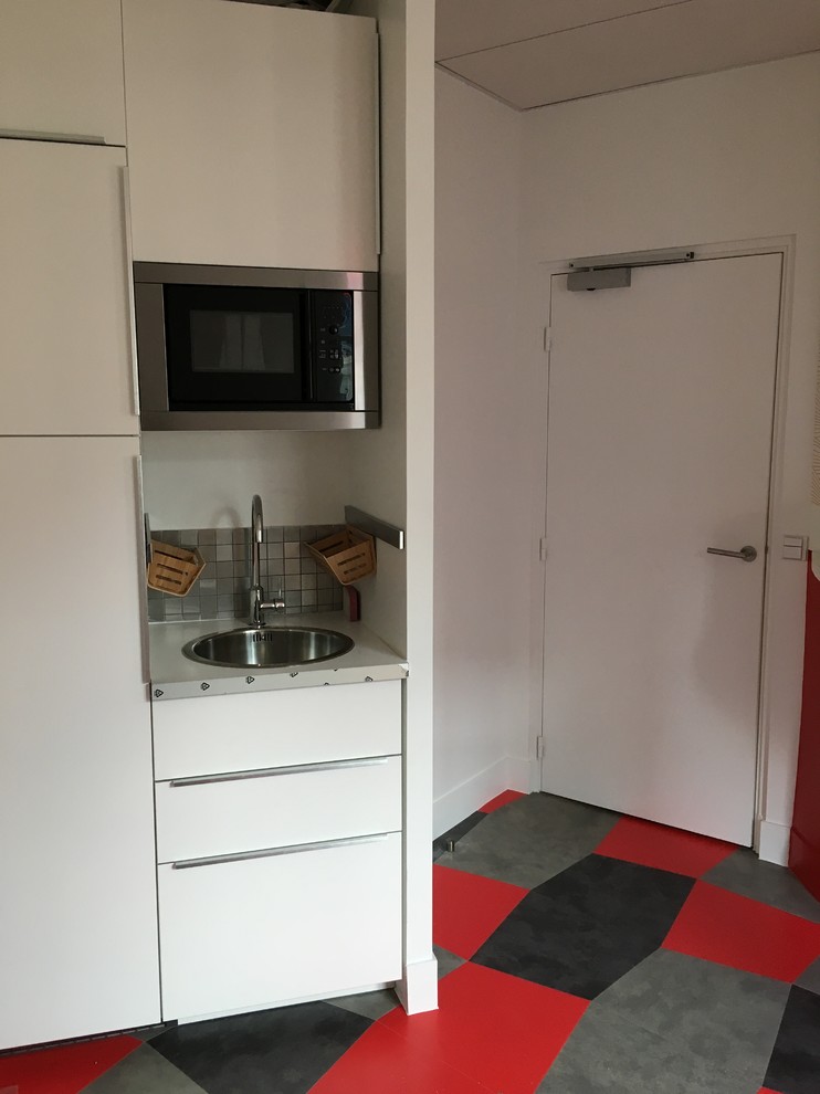 Immagine di una piccola cucina moderna con lavello integrato, paraspruzzi rosso, paraspruzzi con piastrelle in pietra, elettrodomestici in acciaio inossidabile, pavimento in cementine e pavimento grigio