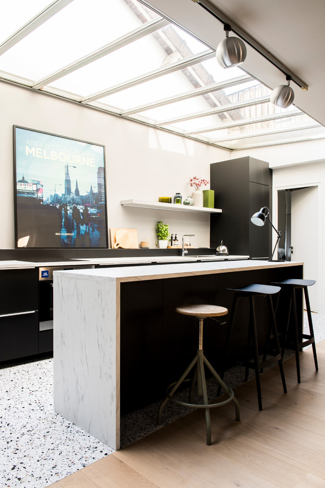 Aménagement d'une cuisine parallèle contemporaine avec un placard à porte plane, des portes de placard noires, parquet clair, îlot, un sol beige, un plan de travail blanc et plafond verrière.