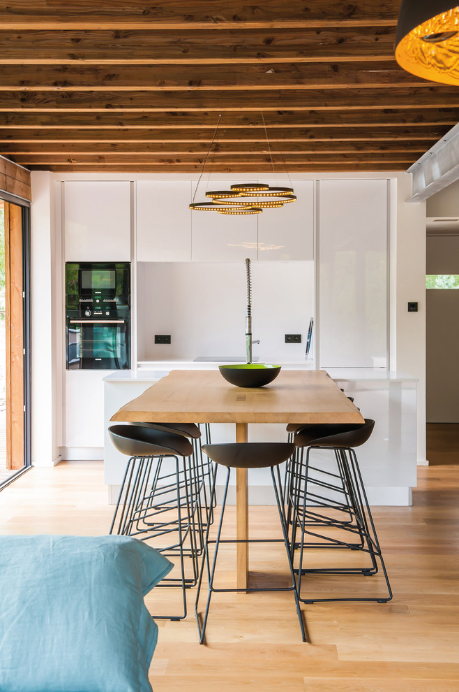 Zweizeilige, Mittelgroße Moderne Wohnküche mit weißen Schränken, Küchenrückwand in Weiß, hellem Holzboden und Kücheninsel in Bordeaux