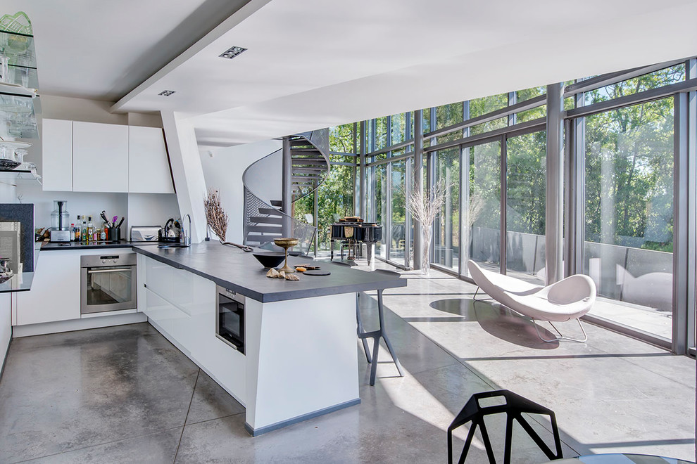 Idéer för ett modernt kök med öppen planlösning, med en enkel diskho, släta luckor, vita skåp, vitt stänkskydd, rostfria vitvaror, betonggolv, en halv köksö och grått golv