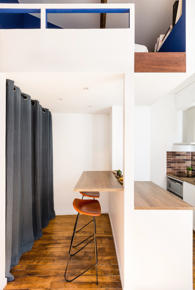 パリにある高級な小さなインダストリアルスタイルのおしゃれなキッチン (フラットパネル扉のキャビネット、白いキャビネット、木材カウンター、茶色いキッチンパネル、シルバーの調理設備、無垢フローリング、茶色い床、茶色いキッチンカウンター、シングルシンク、石タイルのキッチンパネル) の写真