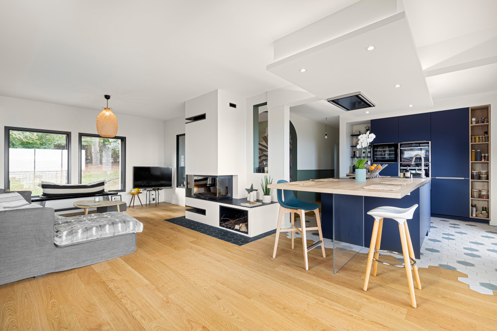 Стильный дизайн: кухня-гостиная в современном стиле с плоскими фасадами, синими фасадами, техникой из нержавеющей стали, островом и бежевой столешницей - последний тренд