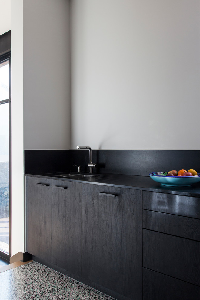 Foto på ett avskilt, mellanstort funkis svart l-kök, med en integrerad diskho, svarta skåp, träbänkskiva, svart stänkskydd, stänkskydd i trä, integrerade vitvaror och terrazzogolv