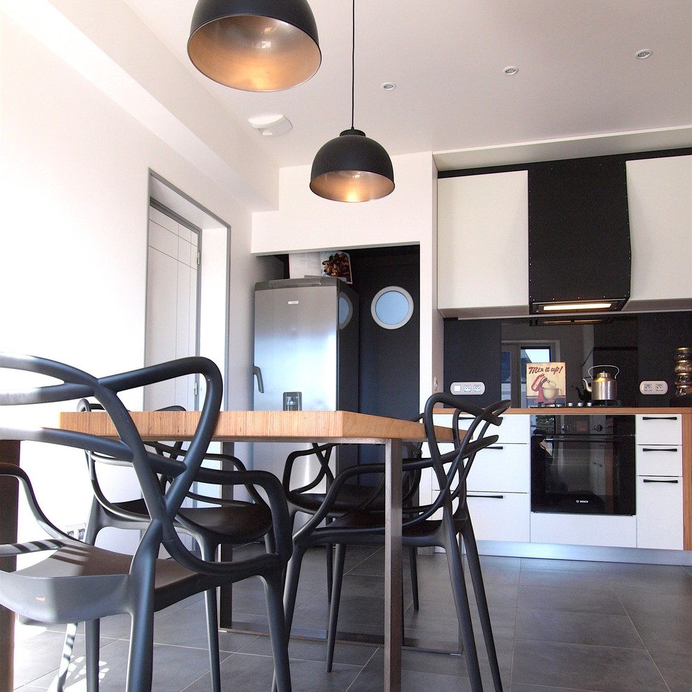 Exempel på ett avskilt, mellanstort modernt l-kök, med en dubbel diskho, luckor med profilerade fronter, vita skåp, träbänkskiva, svart stänkskydd, stänkskydd i skiffer, svarta vitvaror, klinkergolv i keramik och grått golv