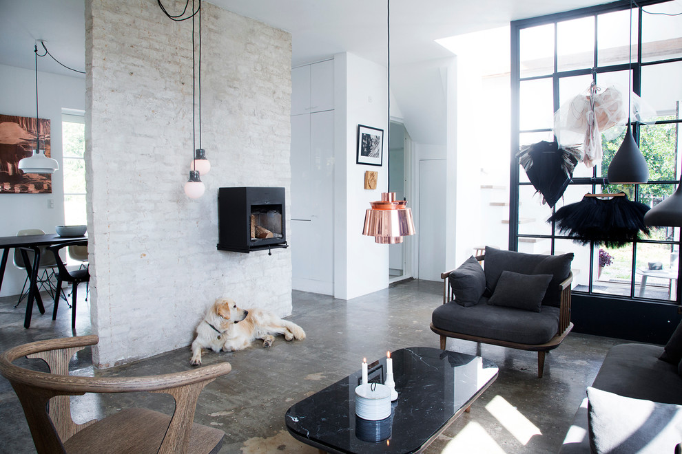 コペンハーゲンにある高級な中くらいな北欧スタイルのおしゃれなリビング (コンクリートの床、薪ストーブ、白い壁、テレビなし、黒いソファ) の写真
