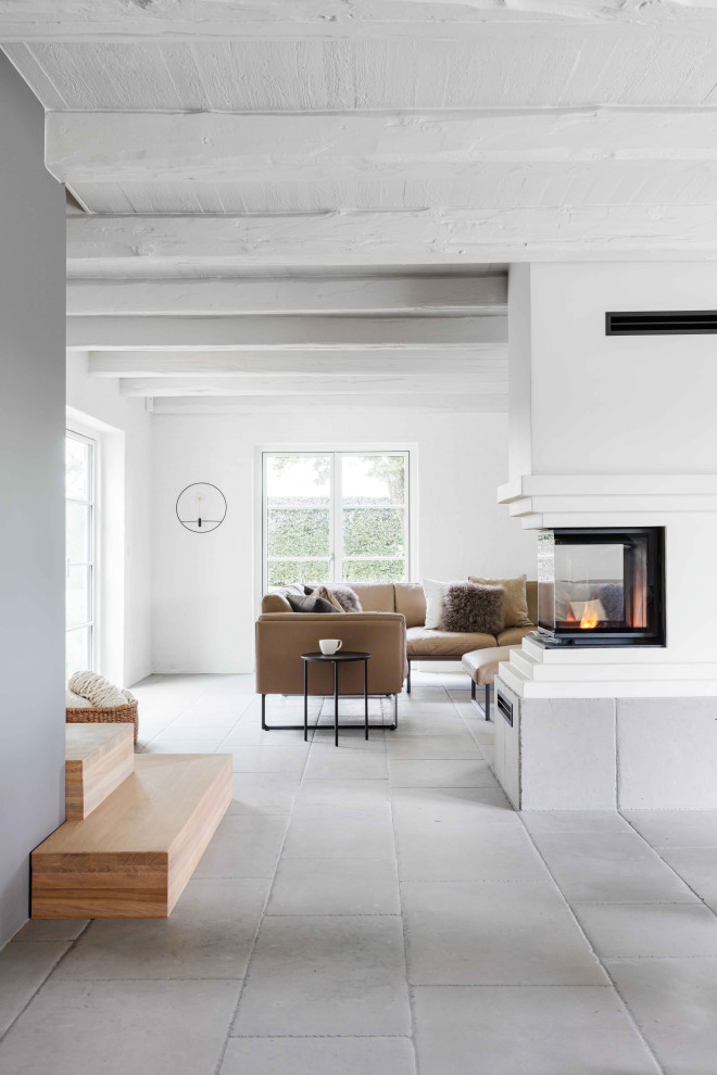 На фото: гостиная комната в скандинавском стиле с белыми стенами, полом из известняка, серым полом и балками на потолке