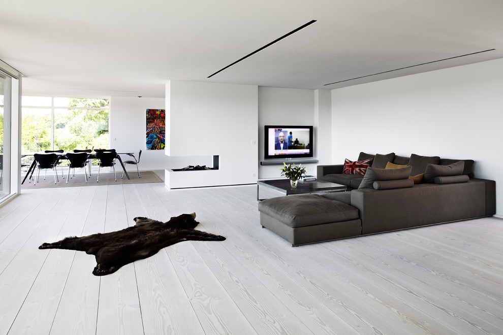 Minimalistisk inredning av ett stort allrum med öppen planlösning, med vita väggar, en väggmonterad TV och vitt golv