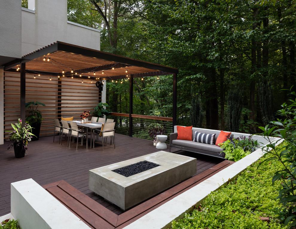 Réalisation d'une grande terrasse arrière design avec un foyer extérieur et une pergola.