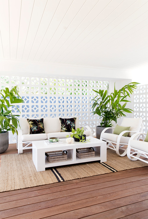 White breeze block wall on a wooden deck behind two white couches a white coffee table and two planters and a rug