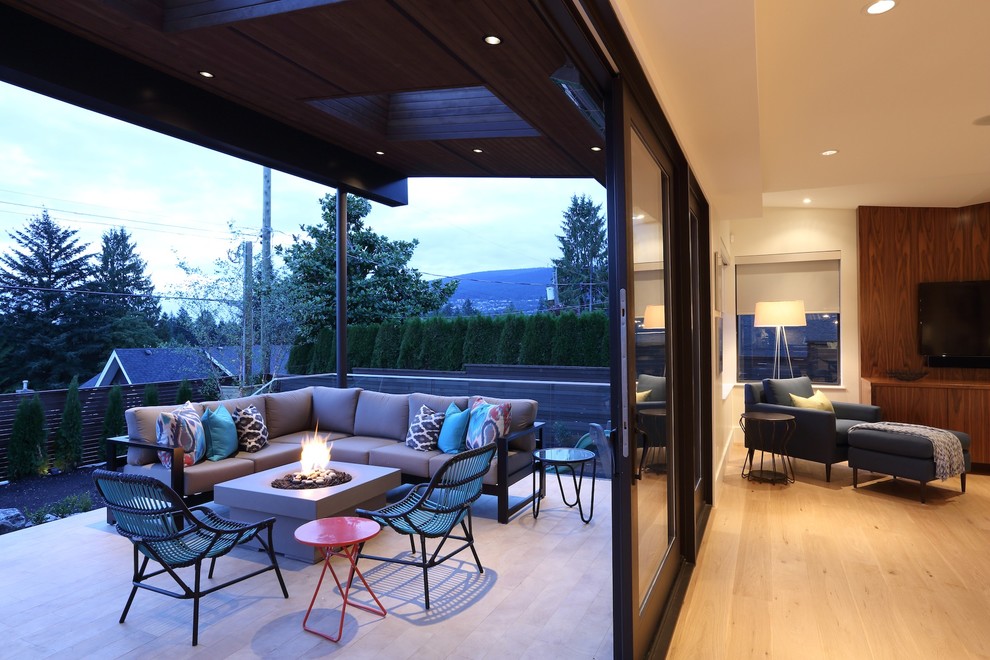 Aménagement d'une grande terrasse arrière contemporaine avec un foyer extérieur et une extension de toiture.