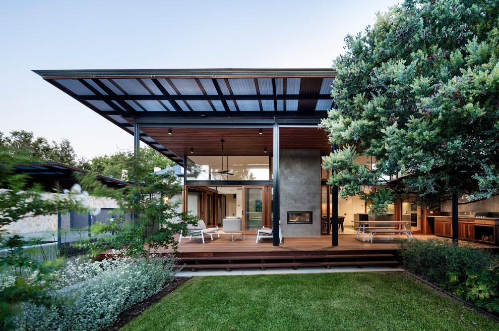 Réalisation d'une terrasse arrière design avec une cuisine d'été et une extension de toiture.
