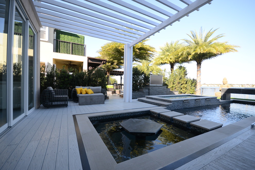 Réalisation d'une très grande terrasse arrière design avec une cuisine d'été et une pergola.
