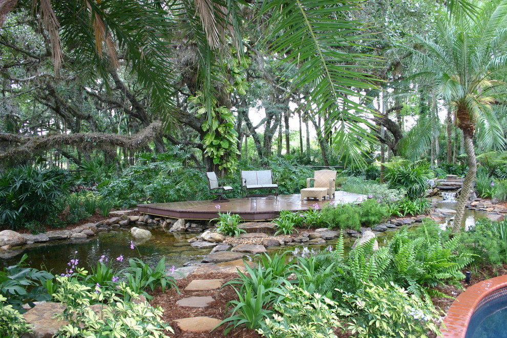 Diseño de terraza tropical sin cubierta en patio trasero con fuente