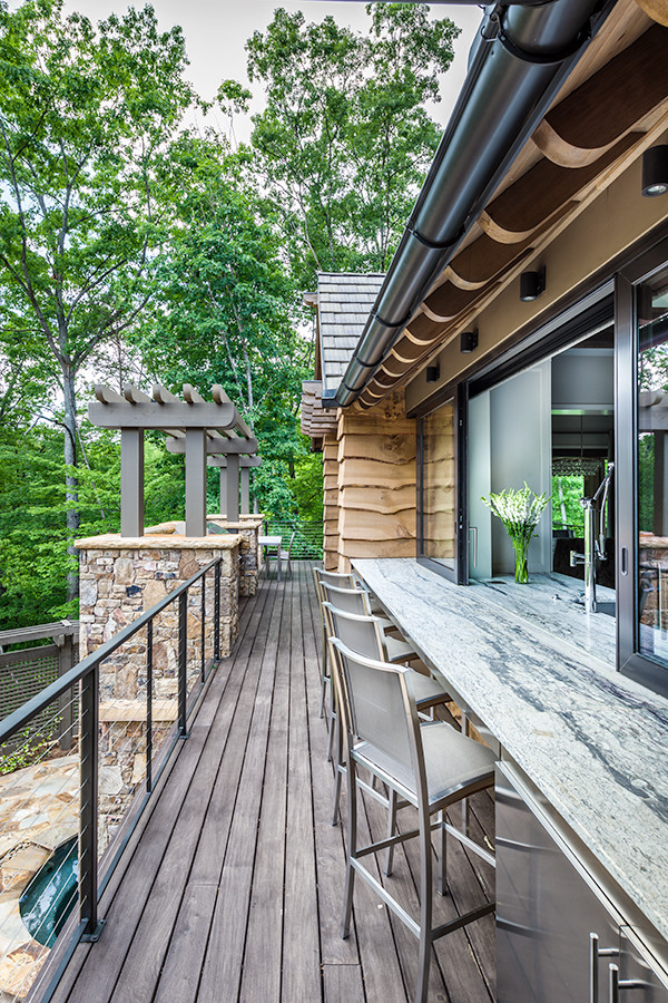 This is an example of a large rustic back terrace in Other with an outdoor kitchen and a roof extension.