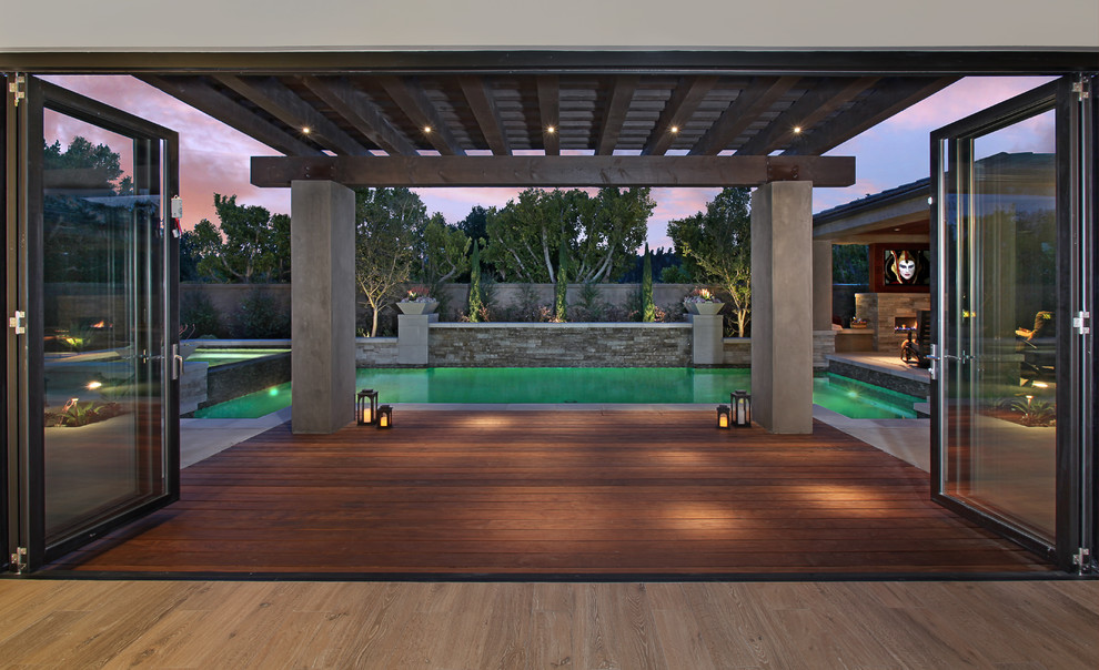 Inspiration for a large contemporary backyard water fountain deck remodel in Orange County with a pergola