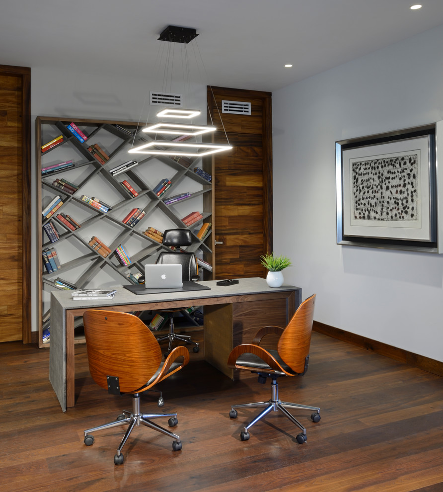 Foto på ett funkis arbetsrum, med ett bibliotek, vita väggar, mellanmörkt trägolv och ett fristående skrivbord