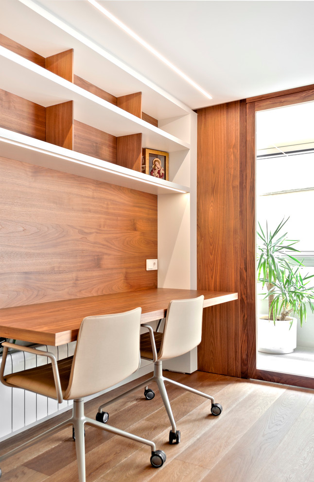Ejemplo de despacho actual pequeño con suelo de madera en tonos medios, escritorio empotrado y paredes blancas