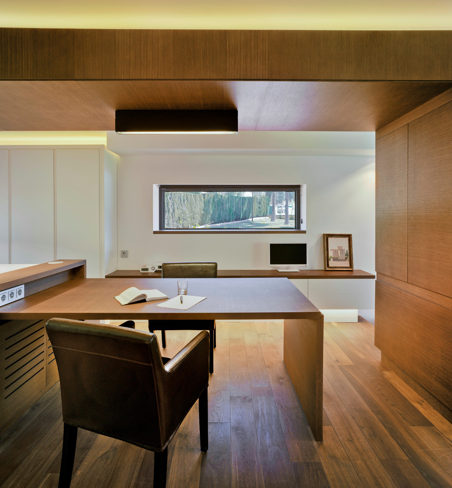 Cette photo montre un bureau moderne de taille moyenne avec un mur blanc, un sol en bois brun et un bureau intégré.