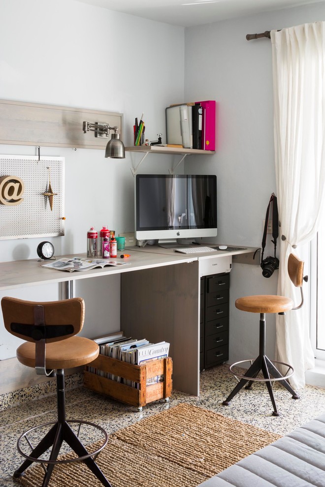 Modelo de despacho ecléctico pequeño sin chimenea con paredes blancas, escritorio independiente y suelo de baldosas de cerámica