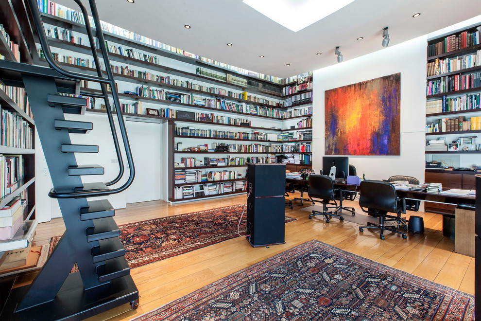 Imagen de despacho actual con biblioteca, paredes blancas, suelo de madera en tonos medios, escritorio independiente y suelo marrón