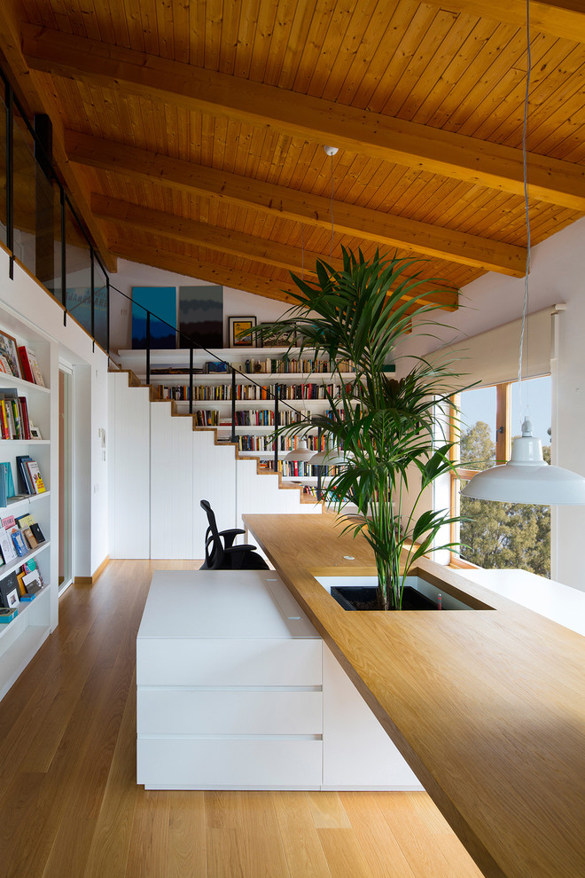 Modern inredning av ett arbetsrum, med ett bibliotek, vita väggar, ljust trägolv, ett inbyggt skrivbord och beiget golv