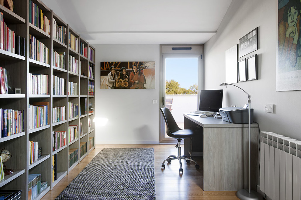 Mittelgroßes Modernes Lesezimmer ohne Kamin mit weißer Wandfarbe, braunem Holzboden, freistehendem Schreibtisch und braunem Boden in Barcelona