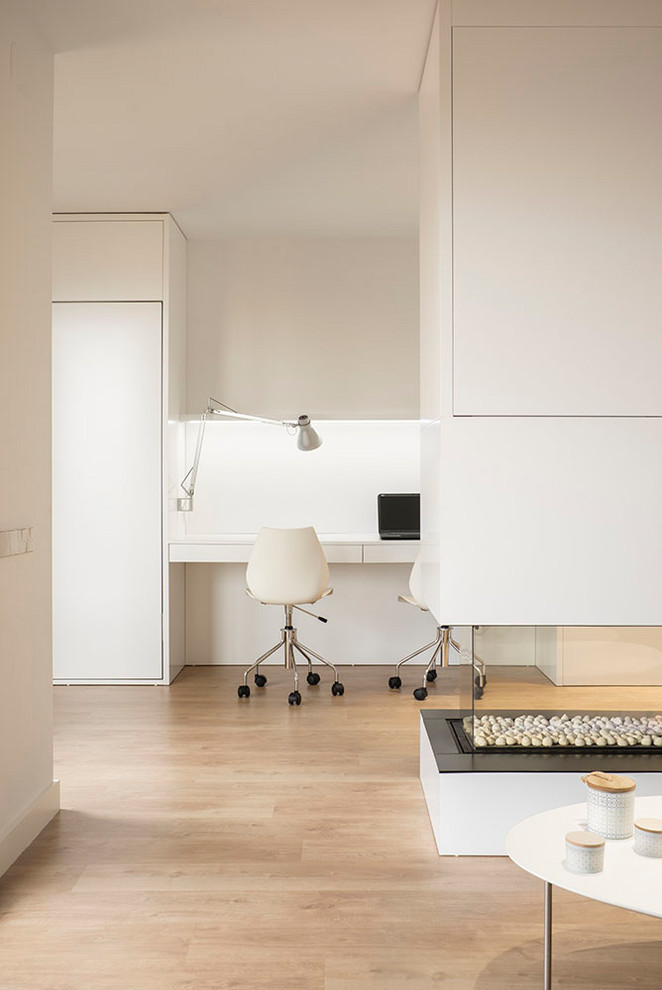 Kleines Skandinavisches Arbeitszimmer mit Arbeitsplatz, weißer Wandfarbe, braunem Holzboden, Tunnelkamin, Einbau-Schreibtisch und braunem Boden in Barcelona