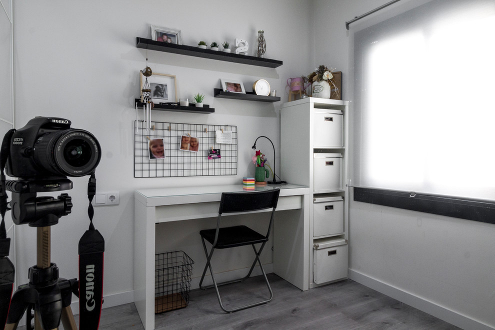 This is an example of a small modern home studio in Barcelona with white walls, laminate floors, a freestanding desk and brown floors.