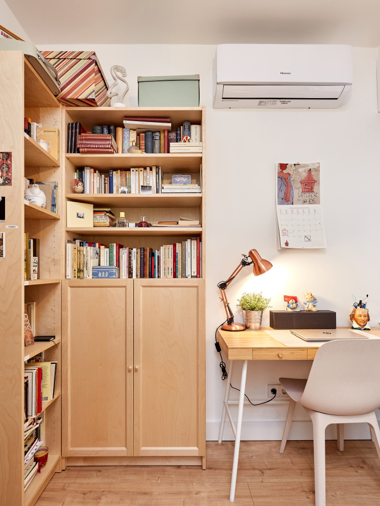 Foto på ett litet skandinaviskt hemmabibliotek, med vita väggar, ljust trägolv, ett fristående skrivbord och beiget golv