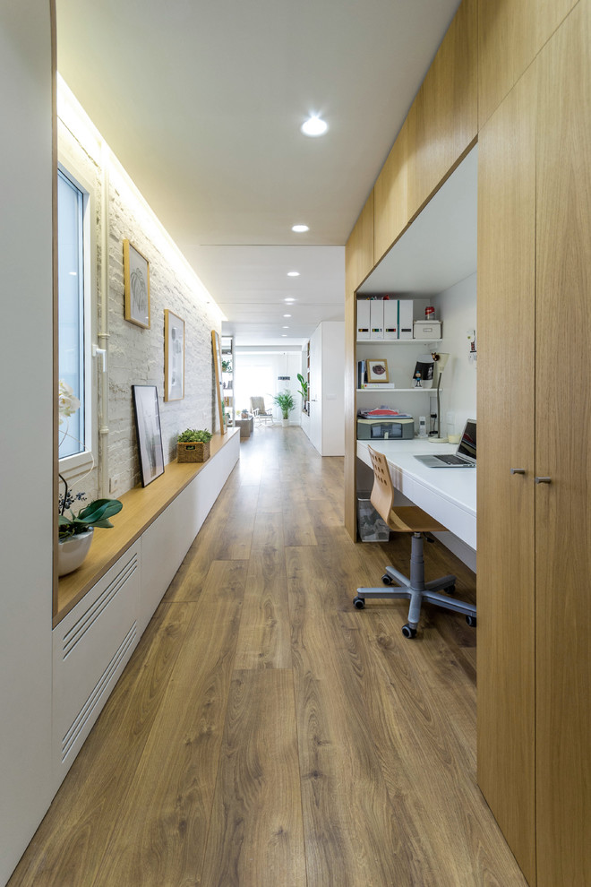 Modernes Arbeitszimmer ohne Kamin mit weißer Wandfarbe, Einbau-Schreibtisch, Arbeitsplatz und hellem Holzboden in Sonstige
