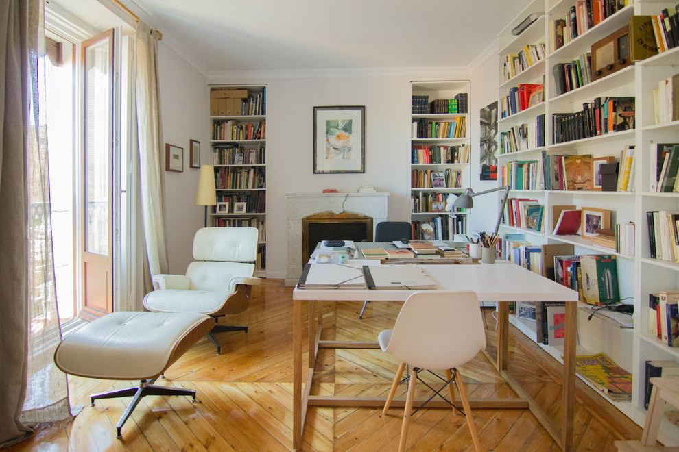 Mittelgroßes Modernes Arbeitszimmer mit Studio, weißer Wandfarbe, braunem Holzboden, Kamin, Kaminumrandung aus Stein, freistehendem Schreibtisch und braunem Boden in Madrid