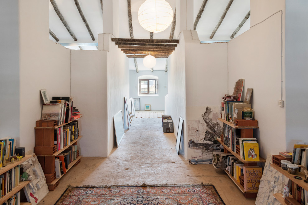 Идея дизайна: домашняя библиотека среднего размера в стиле рустика с белыми стенами, бетонным полом, отдельно стоящим рабочим столом и деревянным потолком