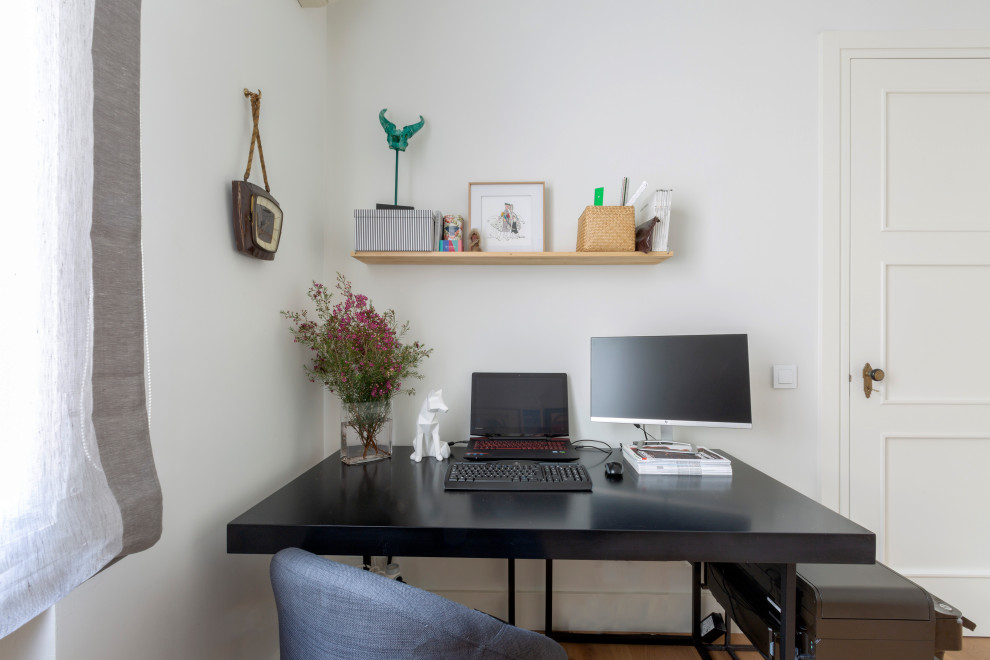 This is an example of a small traditional study in Madrid with white walls, light hardwood flooring and a freestanding desk.
