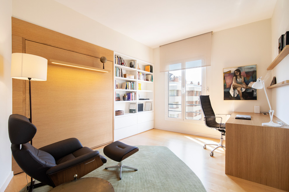 Modelo de despacho actual de tamaño medio con biblioteca, paredes blancas, suelo de madera clara y escritorio independiente