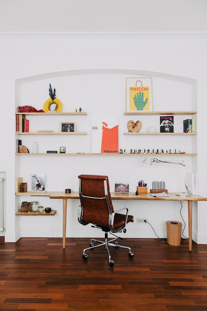 Modelo de despacho retro de tamaño medio sin chimenea con paredes blancas, suelo de madera oscura, escritorio independiente y suelo marrón