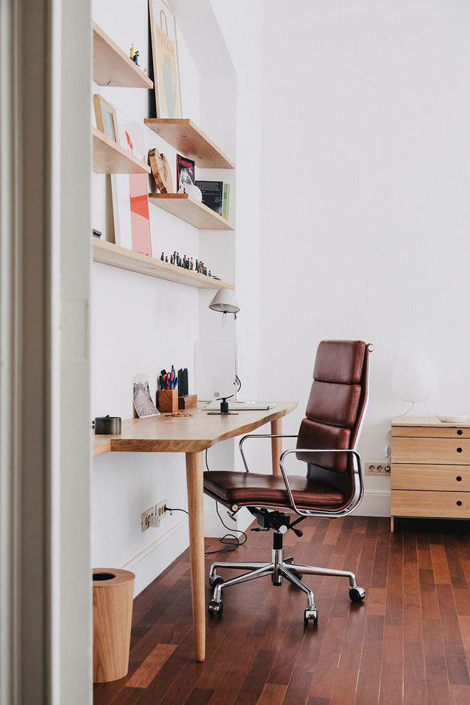 Modelo de despacho retro pequeño sin chimenea con paredes blancas, suelo de madera oscura, escritorio empotrado y suelo marrón