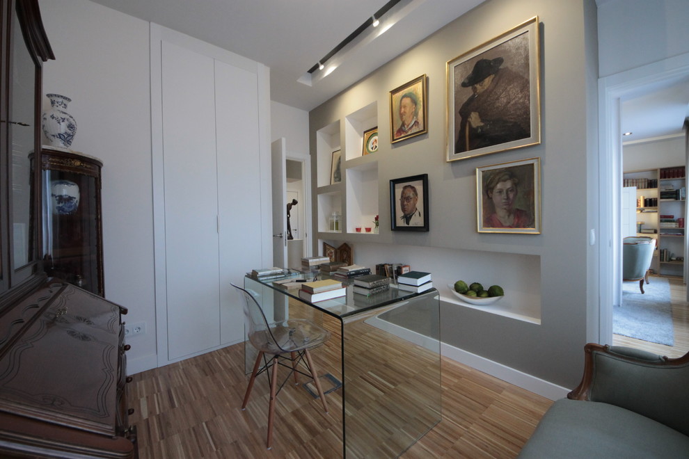 This is an example of a medium sized eclectic home studio in Madrid with grey walls, light hardwood flooring and a freestanding desk.
