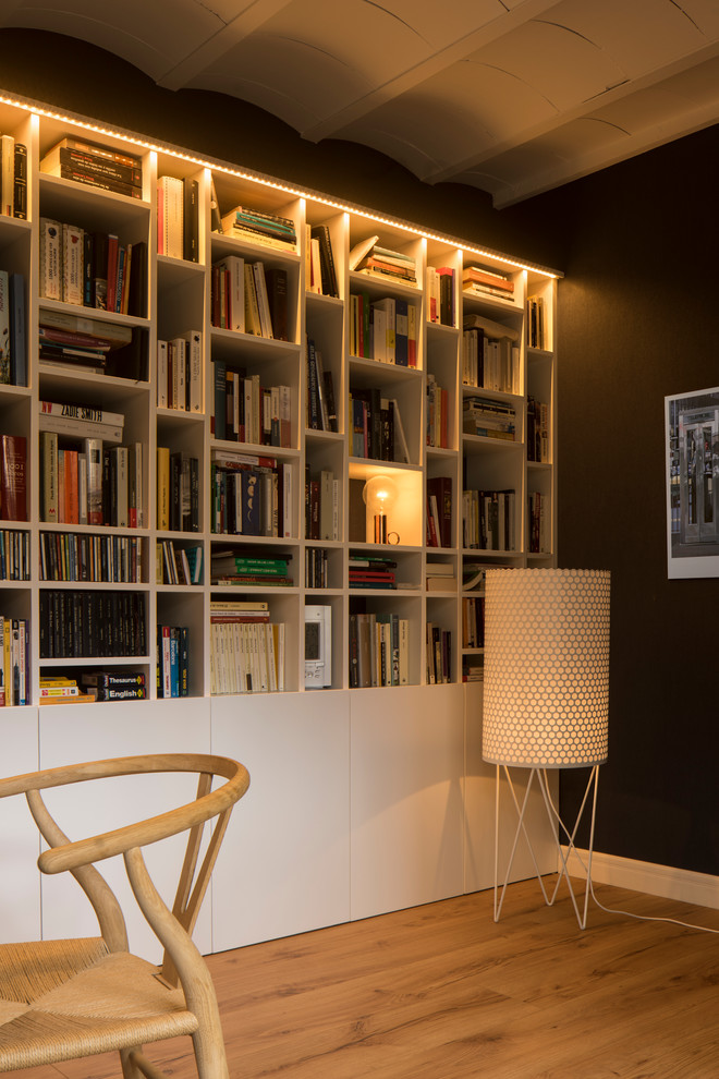 Nordisk inredning av ett mellanstort arbetsrum, med ett bibliotek, vita väggar, mellanmörkt trägolv och ett fristående skrivbord