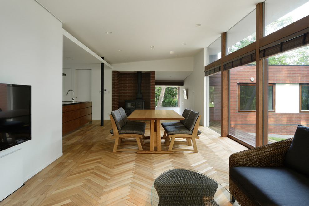 Esempio di una sala da pranzo aperta verso il soggiorno moderna con pareti multicolore, parquet chiaro, stufa a legna e cornice del camino in mattoni