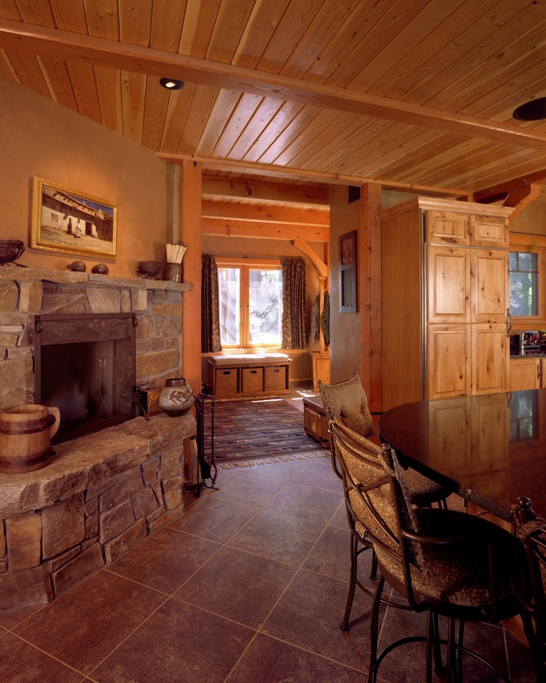 Cette photo montre une salle à manger ouverte sur la cuisine montagne de taille moyenne avec un mur beige, un sol en carrelage de porcelaine, une cheminée standard et un manteau de cheminée en pierre.