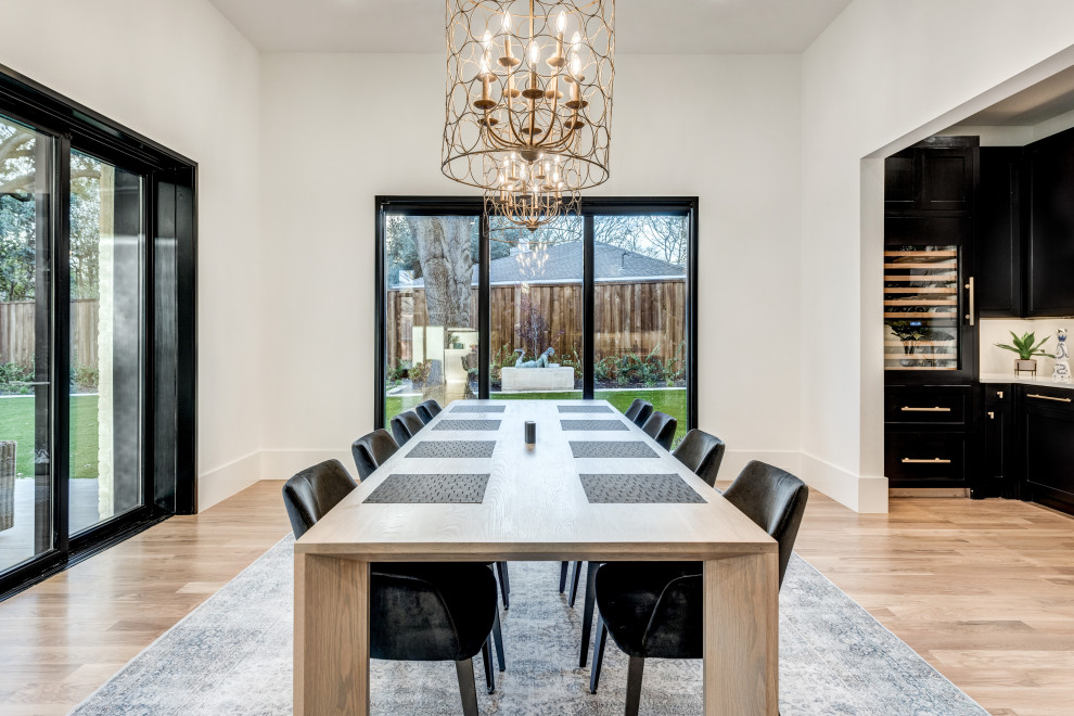 Immagine di una grande sala da pranzo aperta verso la cucina minimalista con pareti bianche, parquet chiaro, nessun camino e pavimento marrone