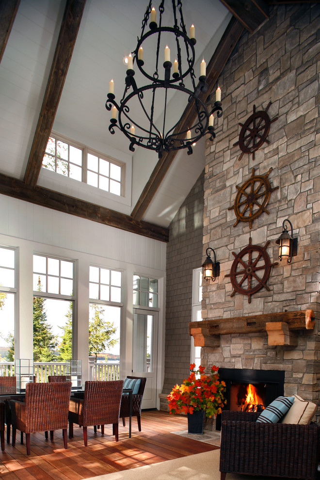 Aménagement d'une grande salle à manger ouverte sur le salon campagne avec un mur blanc, un sol en bois brun, cheminée suspendue, un manteau de cheminée en pierre et un sol marron.