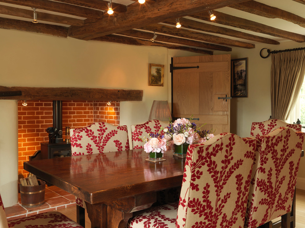 Diseño de comedor de estilo de casa de campo grande cerrado con paredes beige, suelo de madera clara, estufa de leña y marco de chimenea de ladrillo