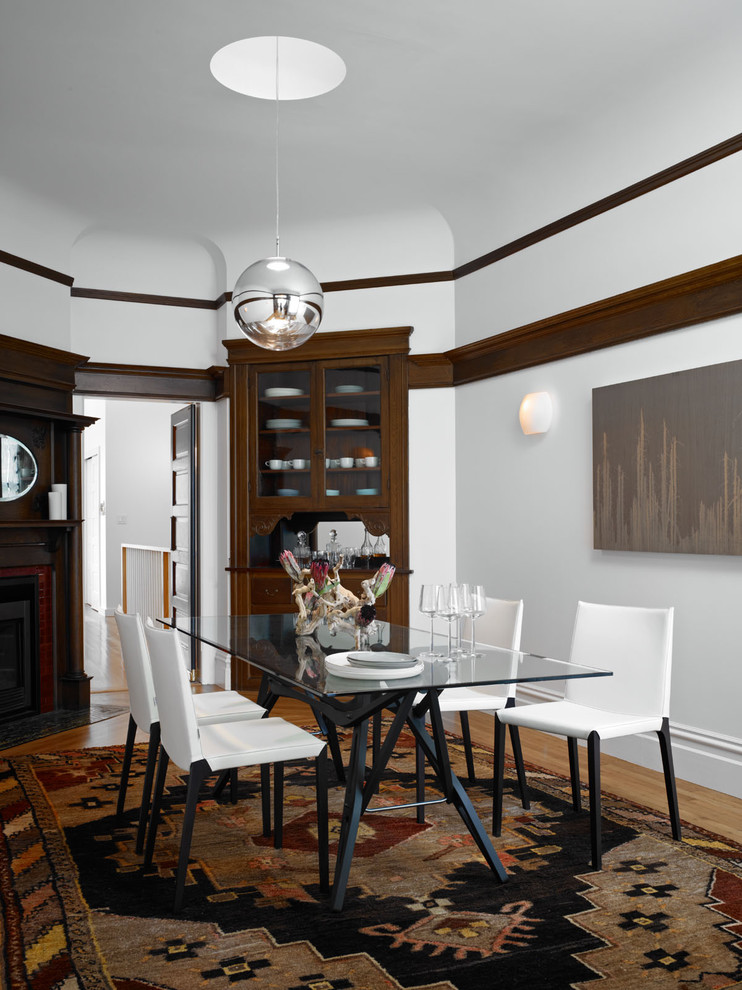 Aménagement d'une salle à manger contemporaine de taille moyenne et fermée avec un mur blanc, une cheminée d'angle et un sol en bois brun.