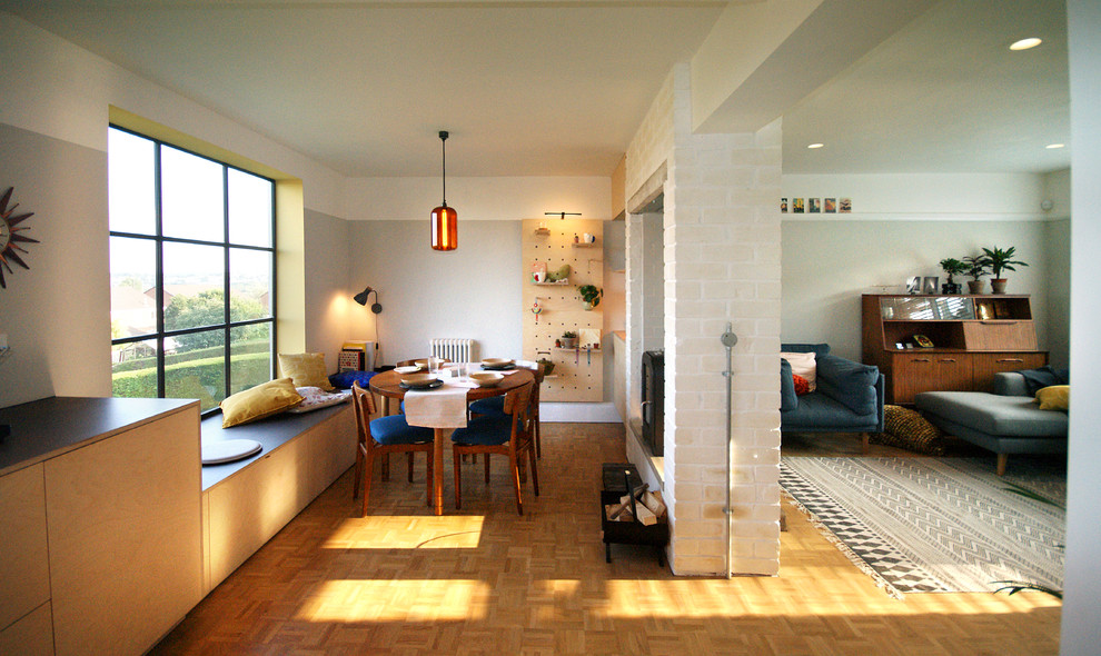 Immagine di una piccola sala da pranzo aperta verso la cucina bohémian con pareti grigie, parquet chiaro, camino bifacciale e cornice del camino in mattoni