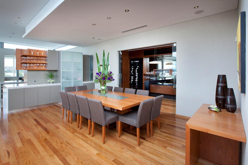 Cette image montre une très grande salle à manger design avec un mur blanc et un sol en bois brun.
