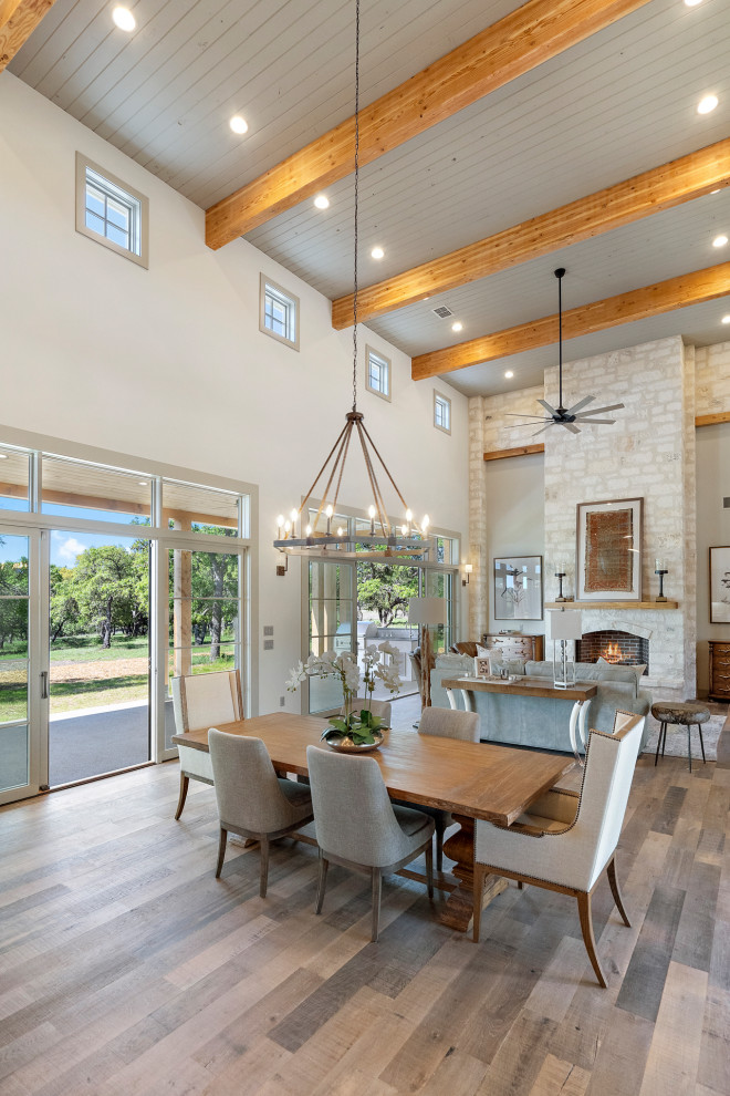 Große Landhaus Wohnküche mit grauer Wandfarbe, hellem Holzboden, Kamin, Kaminumrandung aus Stein, grauem Boden und Holzdecke in Austin